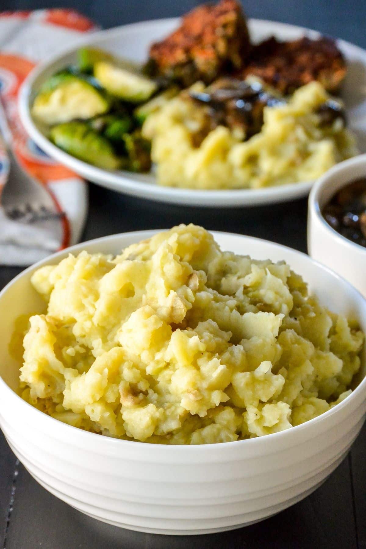 Bowl of mashed potatoes with dinner plate in the background.