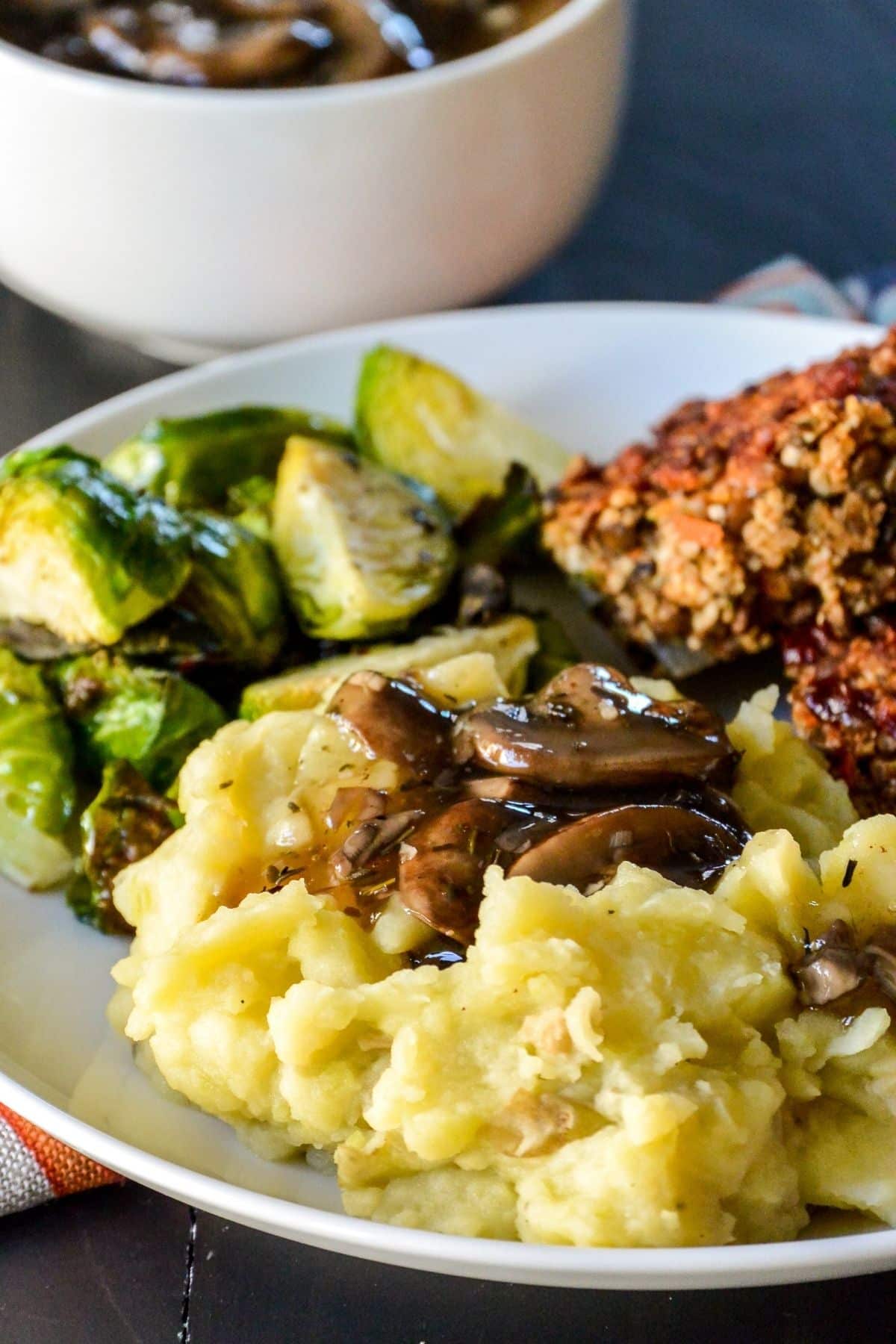 Dinner plate with mashed potatoes topped with mushroom gravy, roasted Brussels sprouts, and lentil meatloaf.