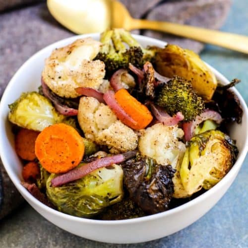 Bowl of roasted vegetables with gold serving spoon.