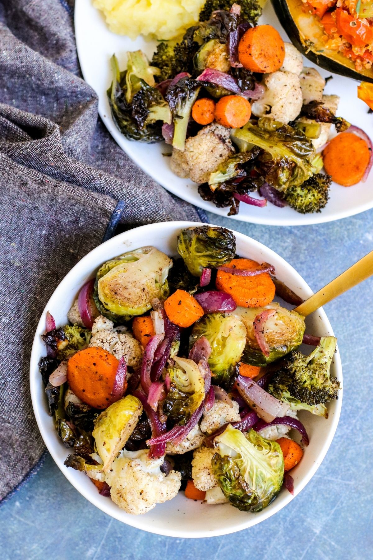 Serving bowl of roasted fall vegetables next to dinner plate.