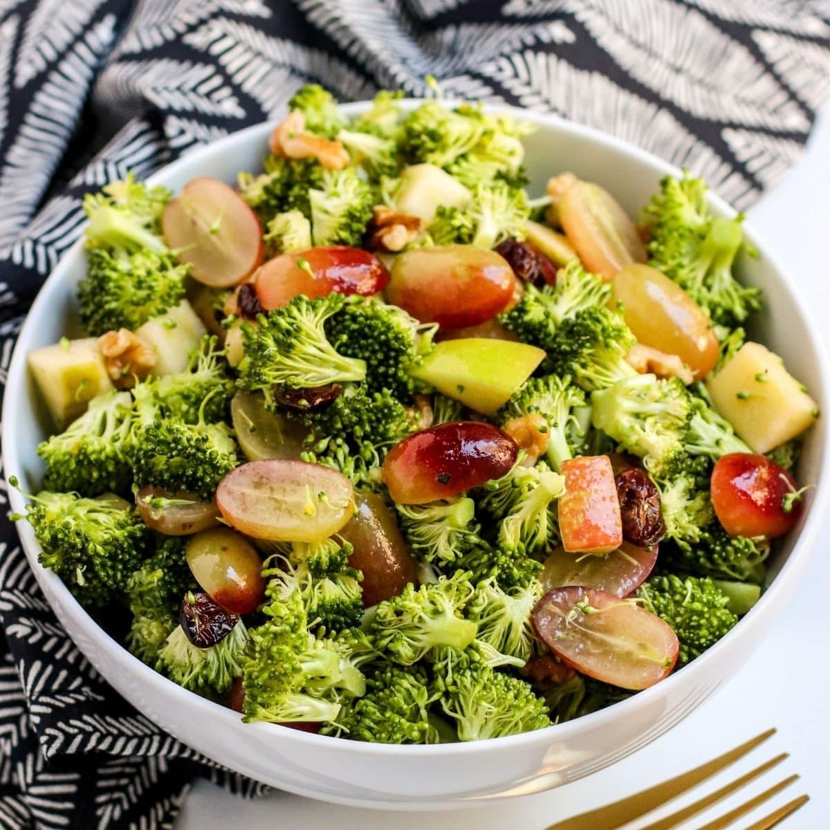 Bowl of broccoli salad with halved grapes and diced apples.