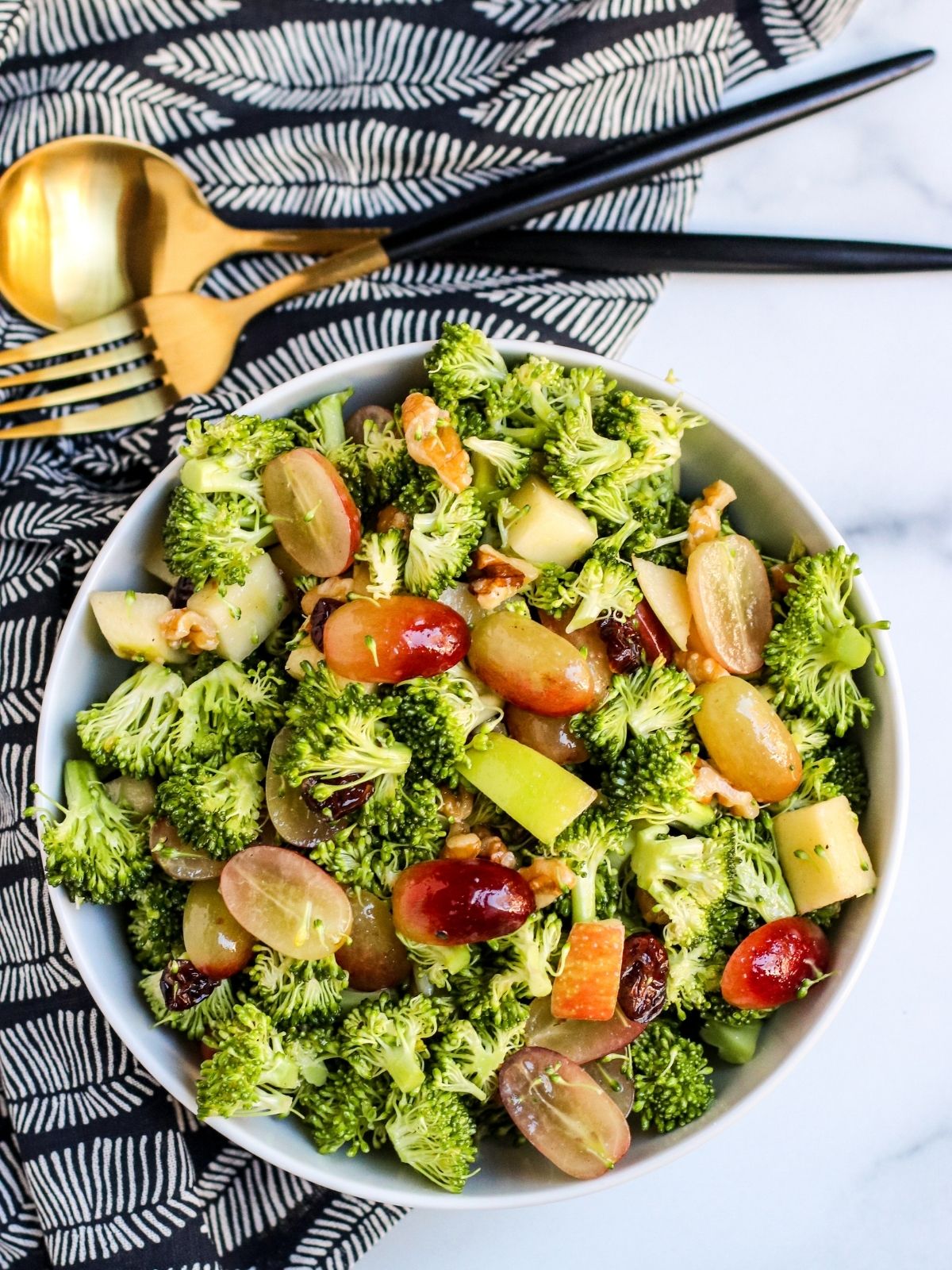 Overhead of bowl of broccoli grape salad with serving utensils.
