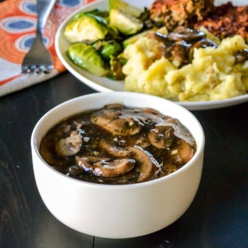 Bowl of mushroom gravy with dinner plate in the background.