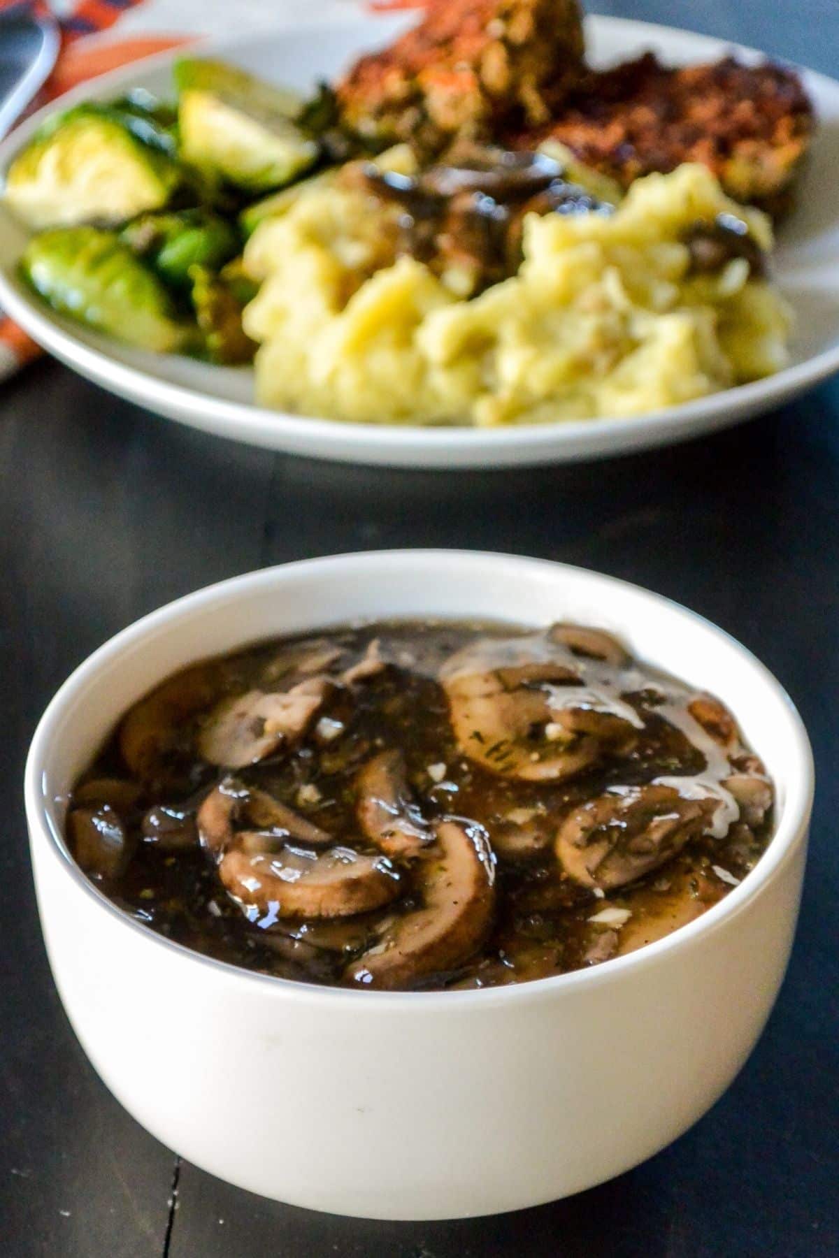 Bowl of gravy in foreground and dinner plate with mashed potatoes and gravy in background.