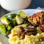 Dinner plate with mashed potatoes, mushroom gravy, roasted Brussels sprouts, and lentil meatloaf with bowl of gravy in the background.