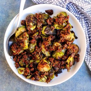 Bowl of roasted Brussels sprouts topped with sun-dried tomato pesto.