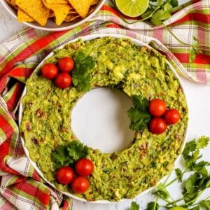 Guacamole served in the shape of a Christmas wreath garnished with cherry tomatoes and cilantro.