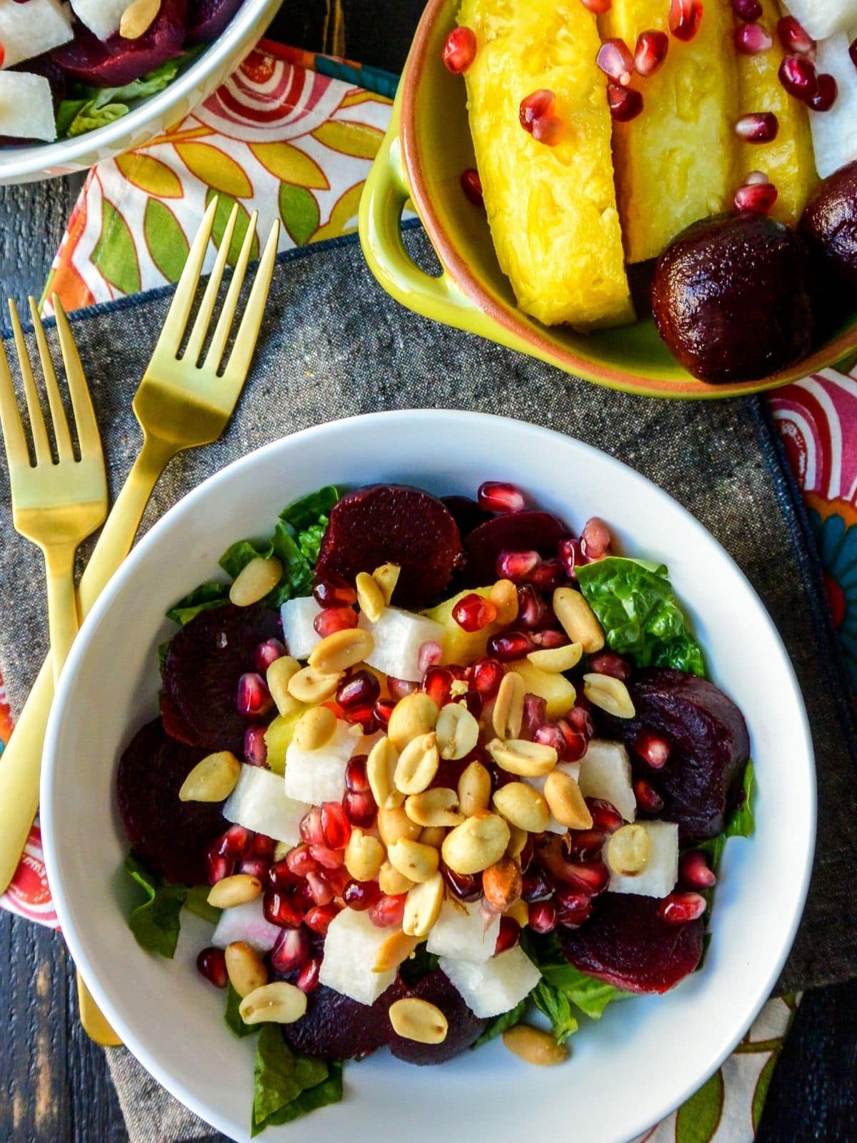 Salad next to bowl of pineapple spears, jicama, beets, and pomegranate seeds.