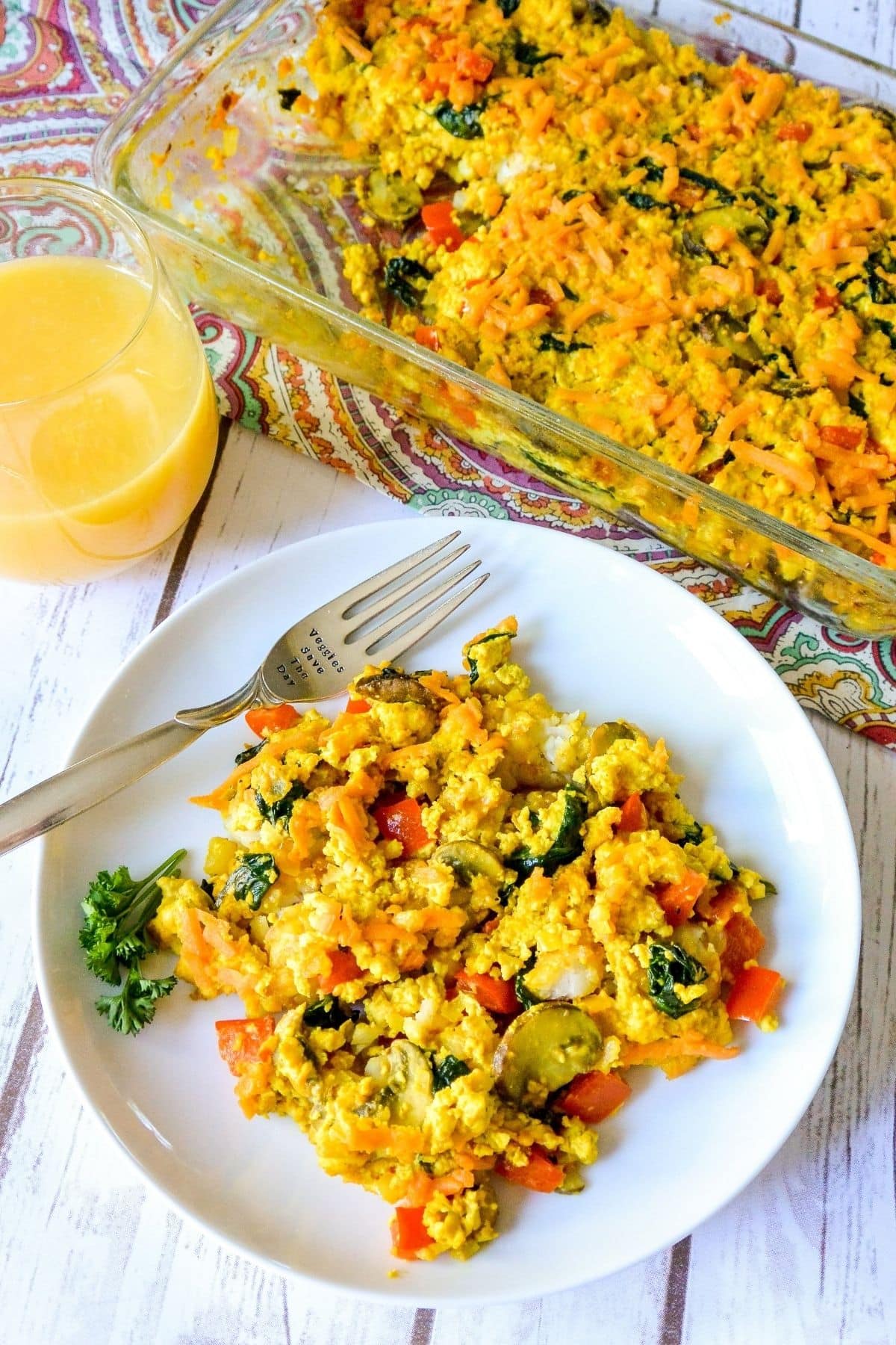 Serving of casserole on a plate with casserole dish and glass of orange juice in the background.