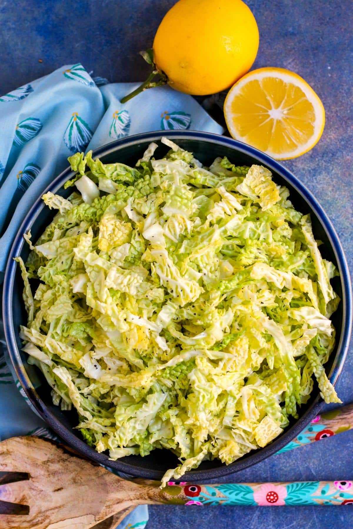 Slaw in a serving bowl with cut lemon and serving spoons next to it.