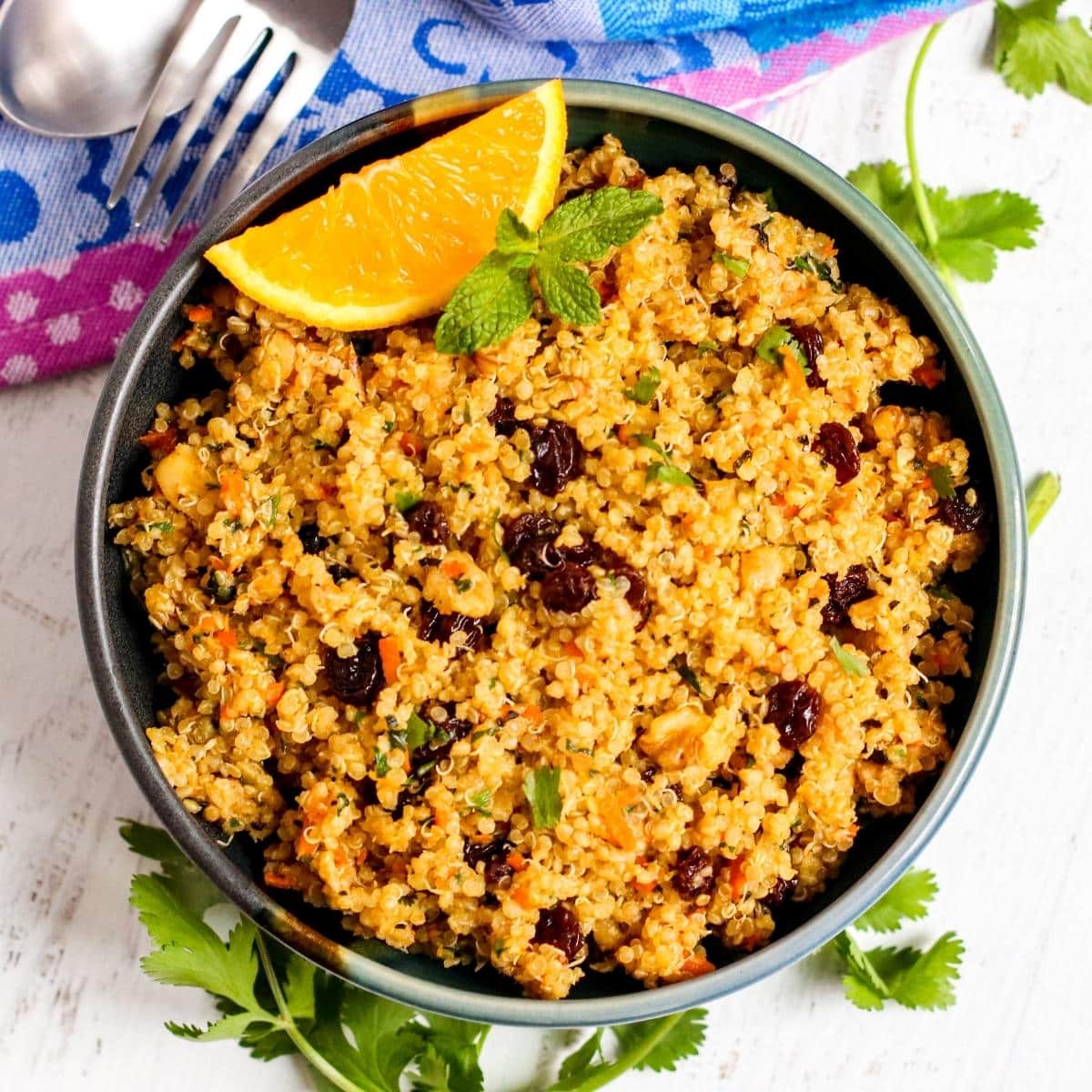 Serving bowl of spiced quinoa garnished with an orange wedge and sprig of mint.