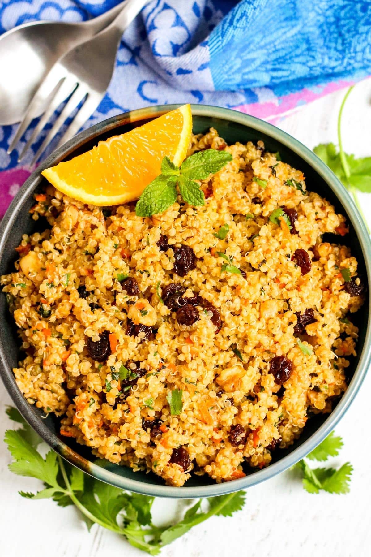 Serving bowl of quinoa garnished with an orange wedge and sprig of fresh mint.