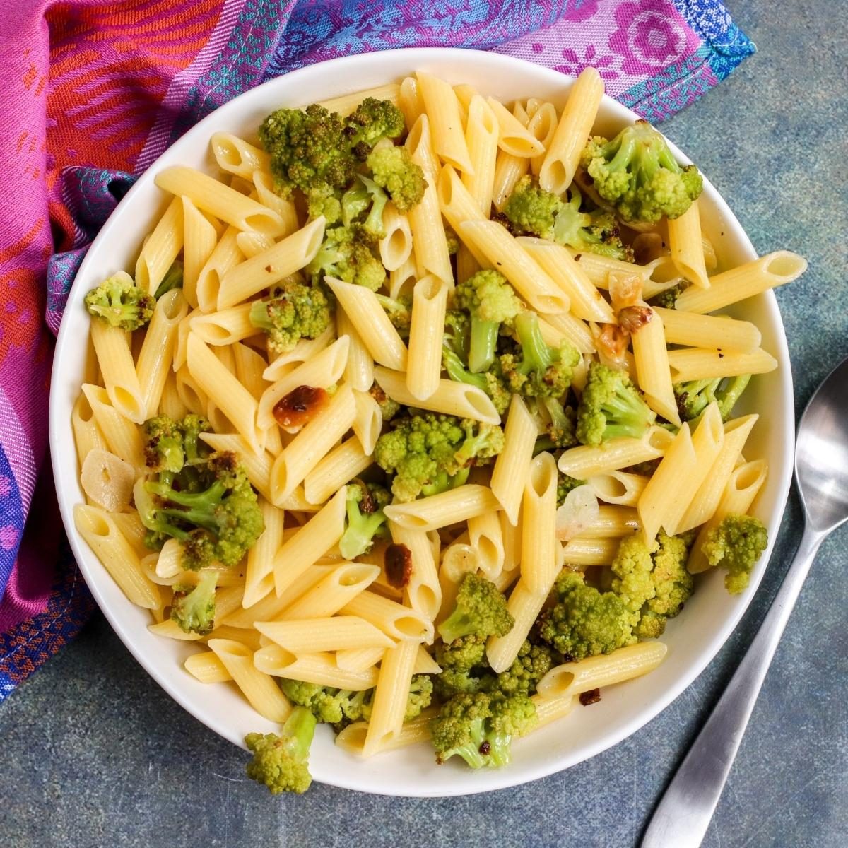 Bowl of penne pasta with roasted garlic and Romanesco florets.