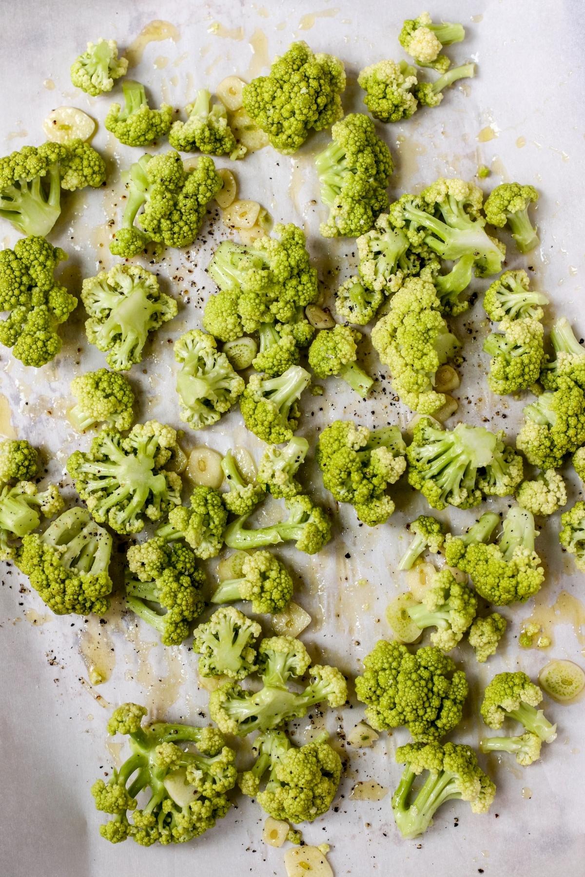 Romanesco florets and garlic slices on a parchment paper lined baking sheet.
