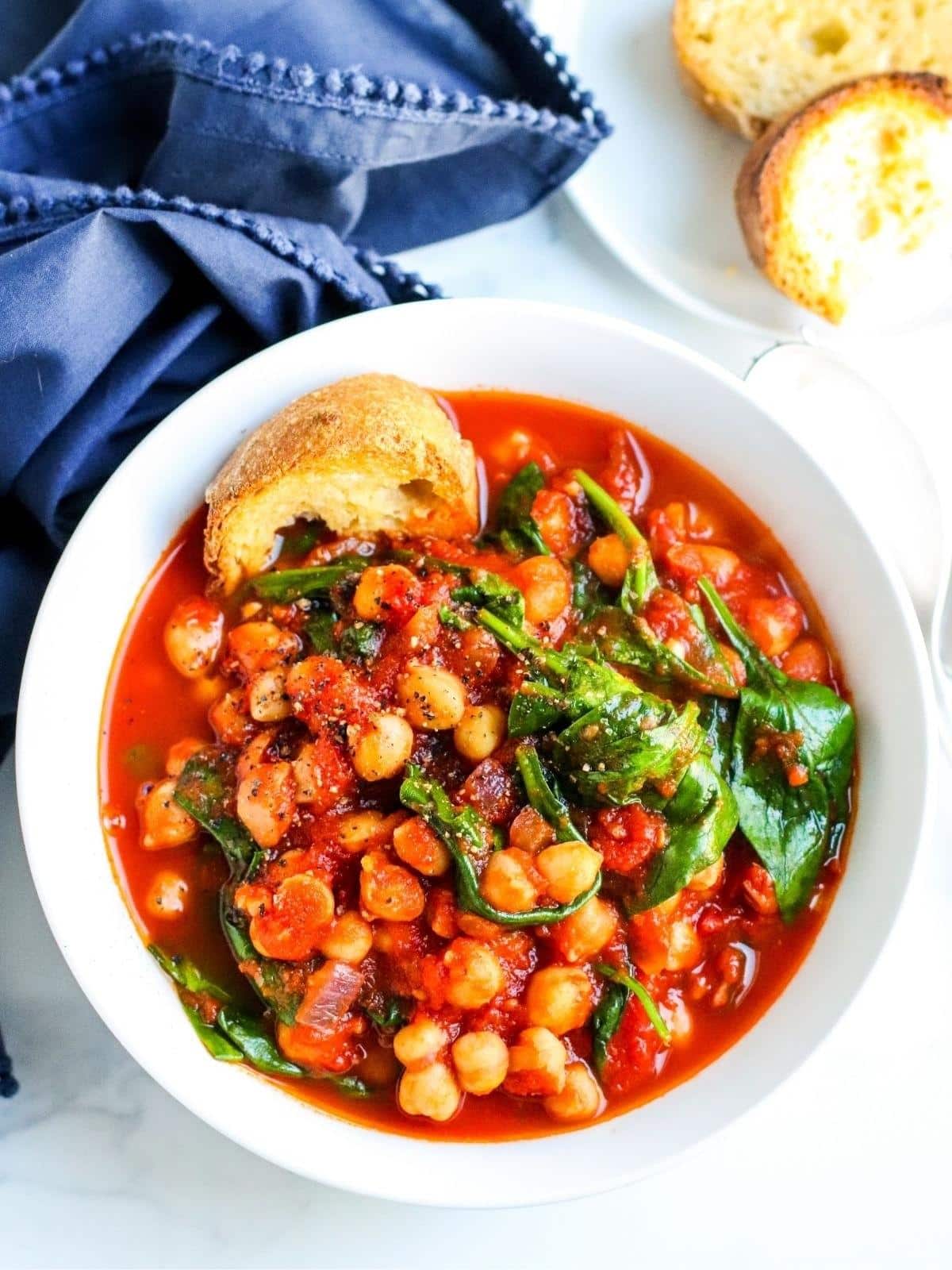 Bowl of Spanish Chickpea Stew with a piece of baguette in it.