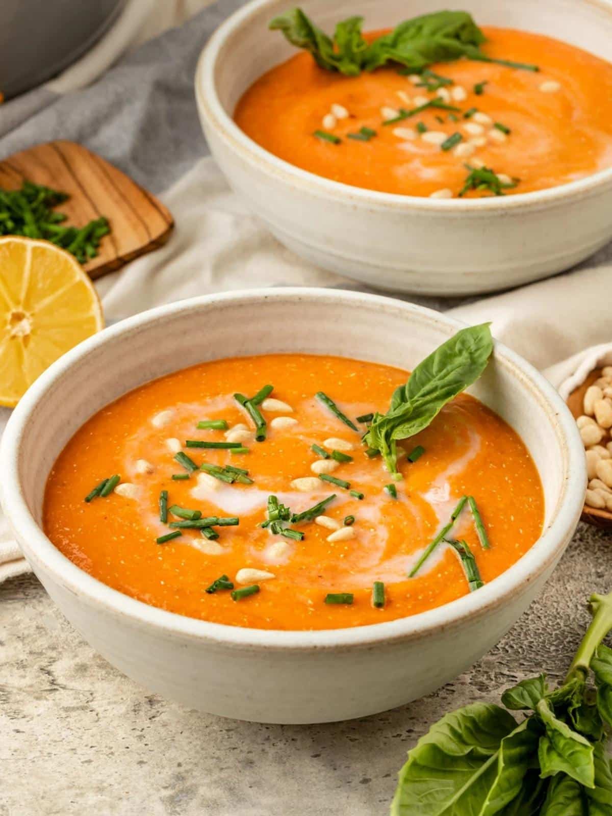 Bowl of red pepper soup garnished with chives and basil.