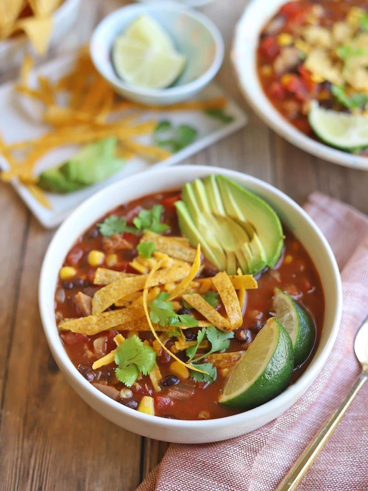 Bowl of tortilla soup garnished with avocado and limes.