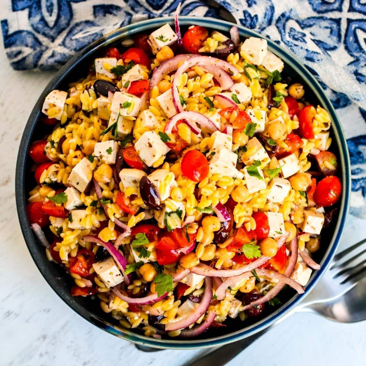 Bowl of Mediterranean Vegan Orzo Salad next to blue and white napkin.