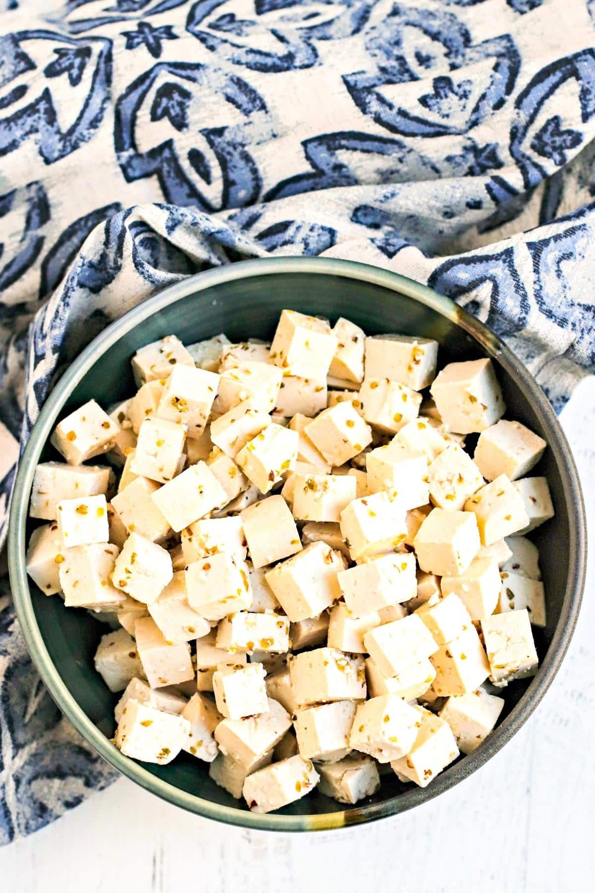 Bowl of tofu feta next to blue and white napkin.