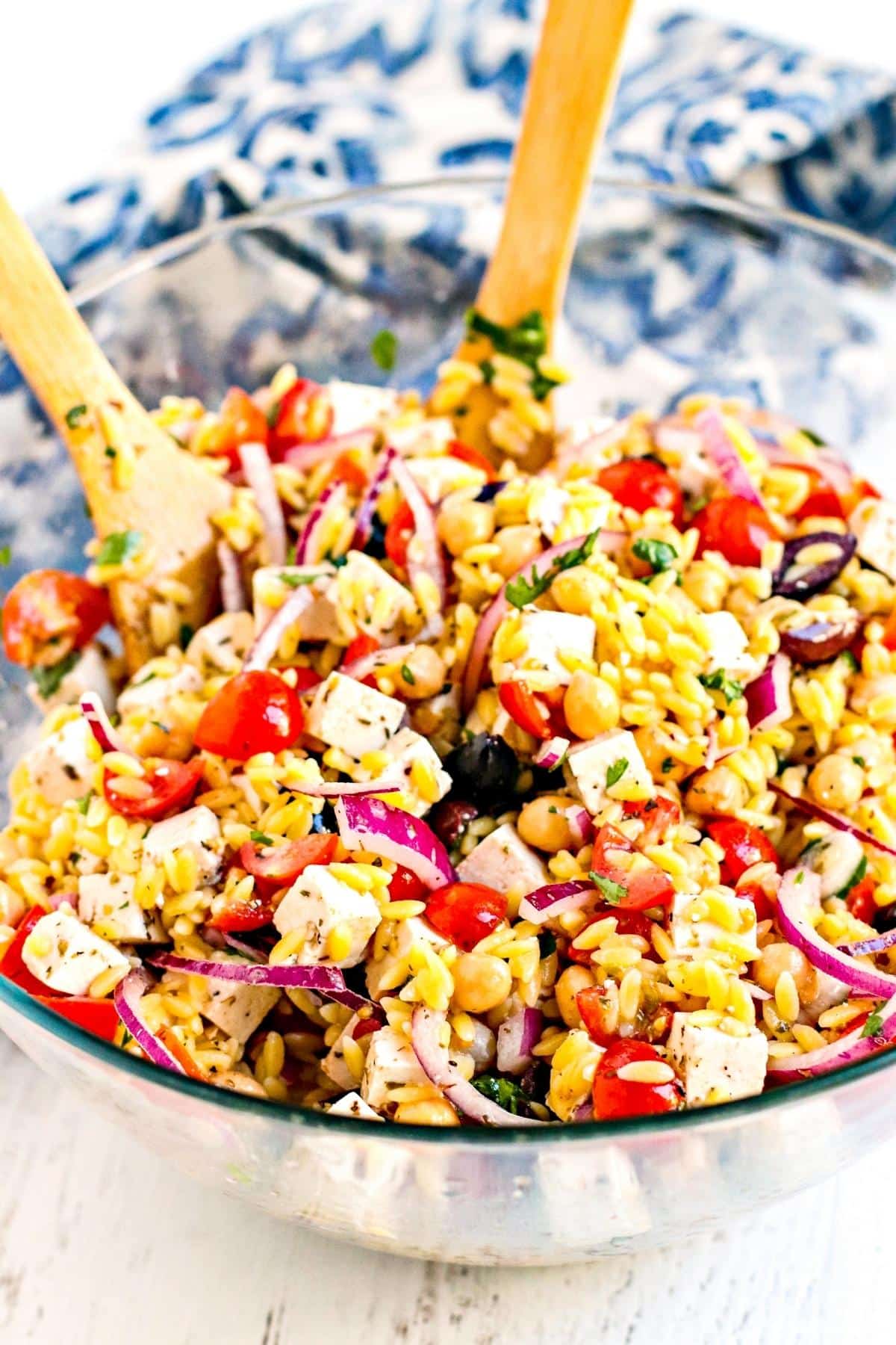 Orzo salad tossed in a mixing bowl with wooden utensils.