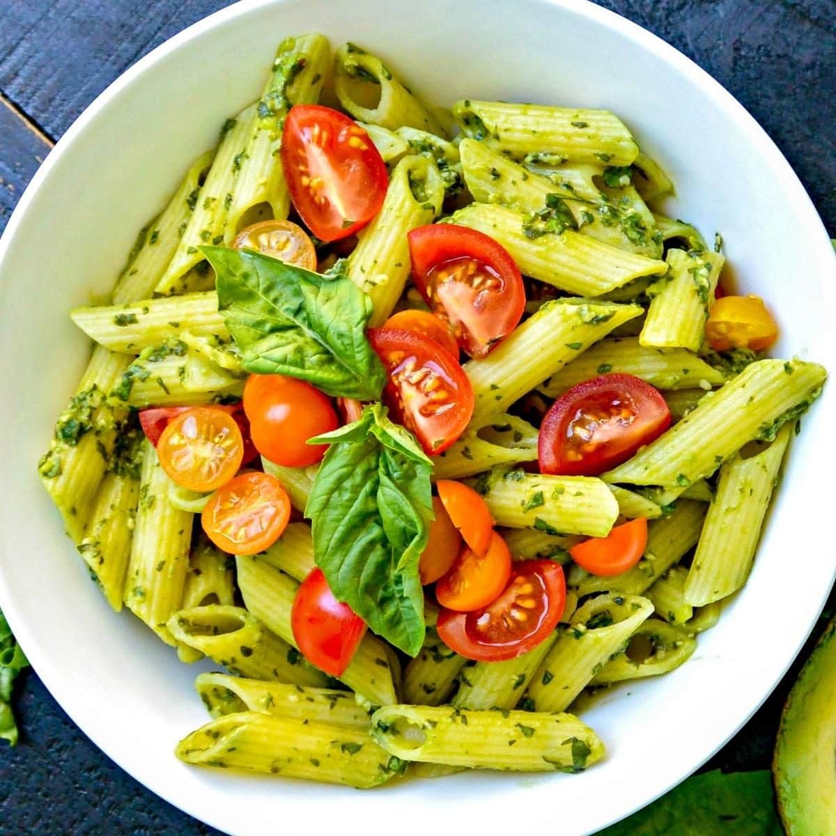 Bowl of penne tossed with vegan avocado sauce and topped with cherry tomato halves.