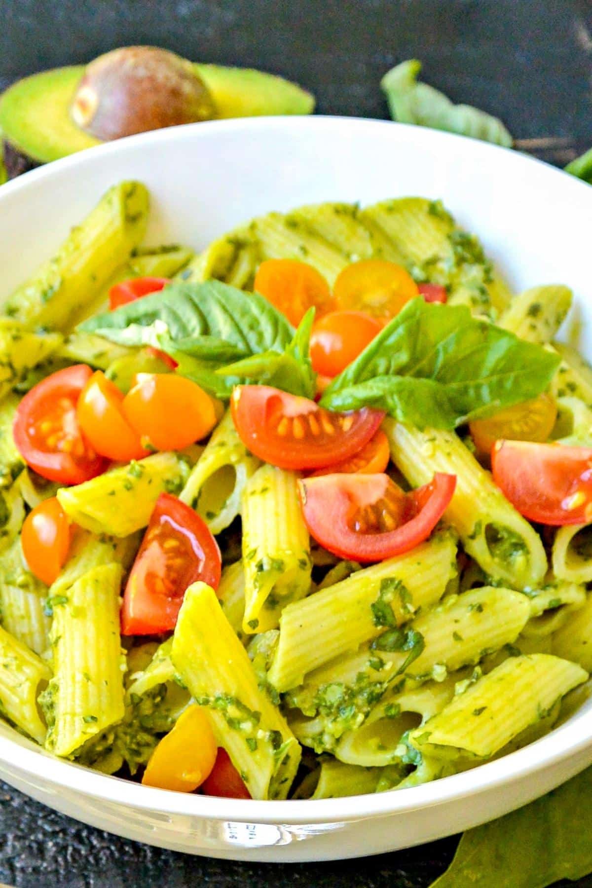 Close up of bowl of penne tossed with vegan avocado pasta sauce and topped with quartered cherry tomatoes.