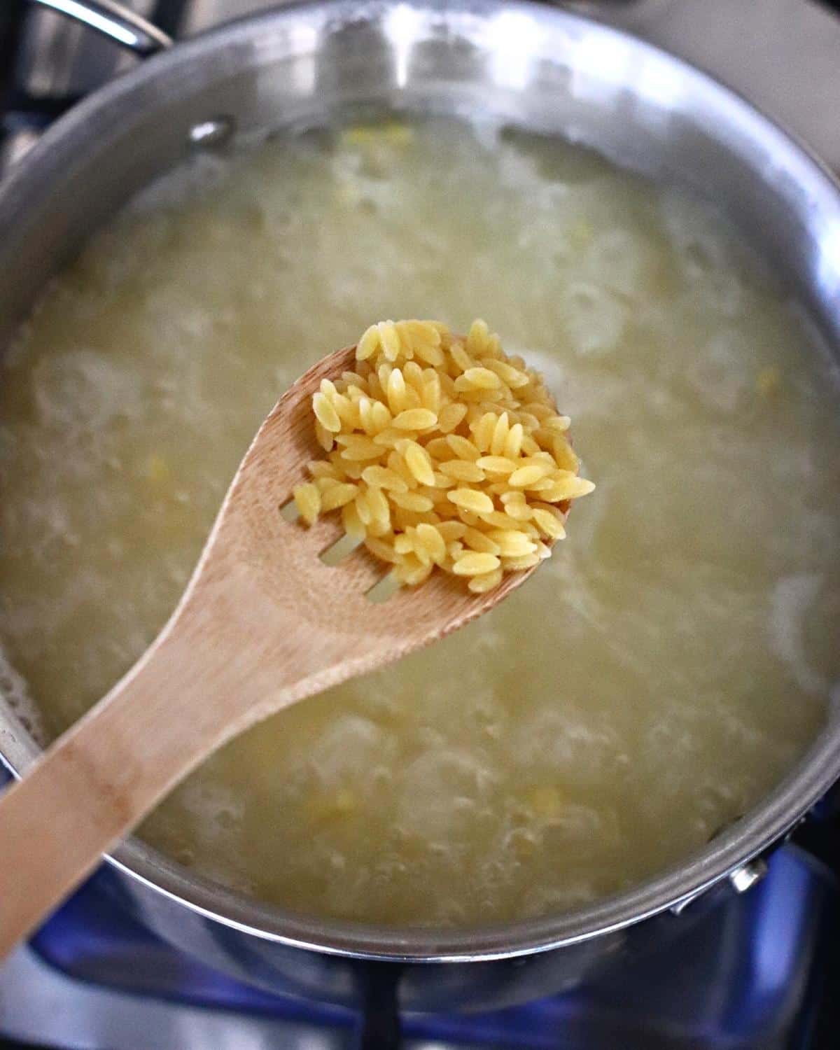 Wooden spoon with cooked orzo over a pot of simmering water.