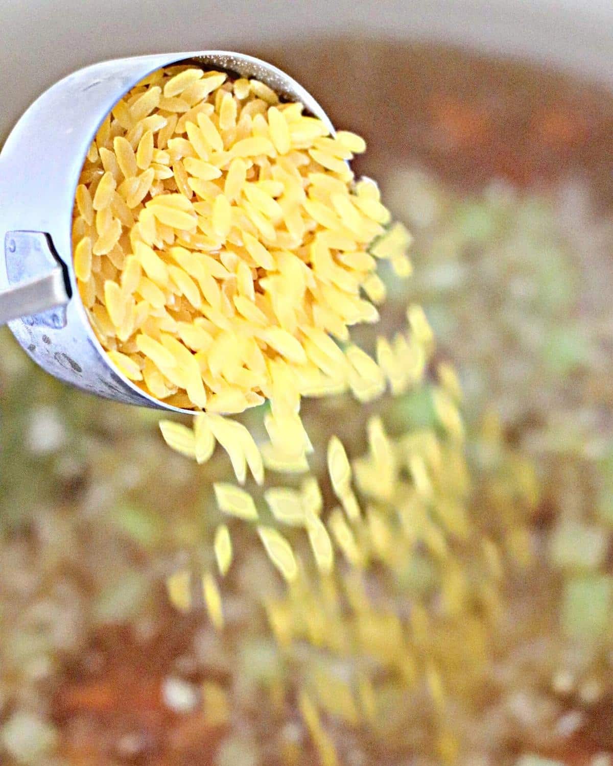 Cup of orzo being poured into a pot of cooking soup.