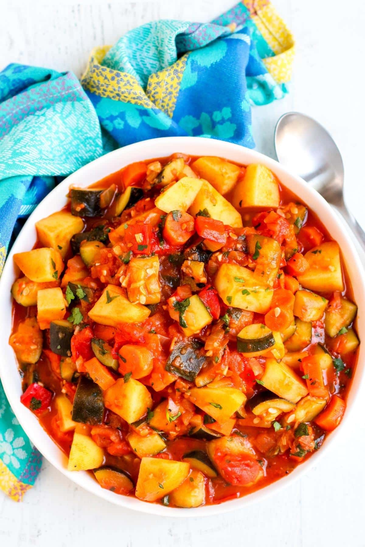 Bowl of zucchini stew with blue napkin and serving spoon.