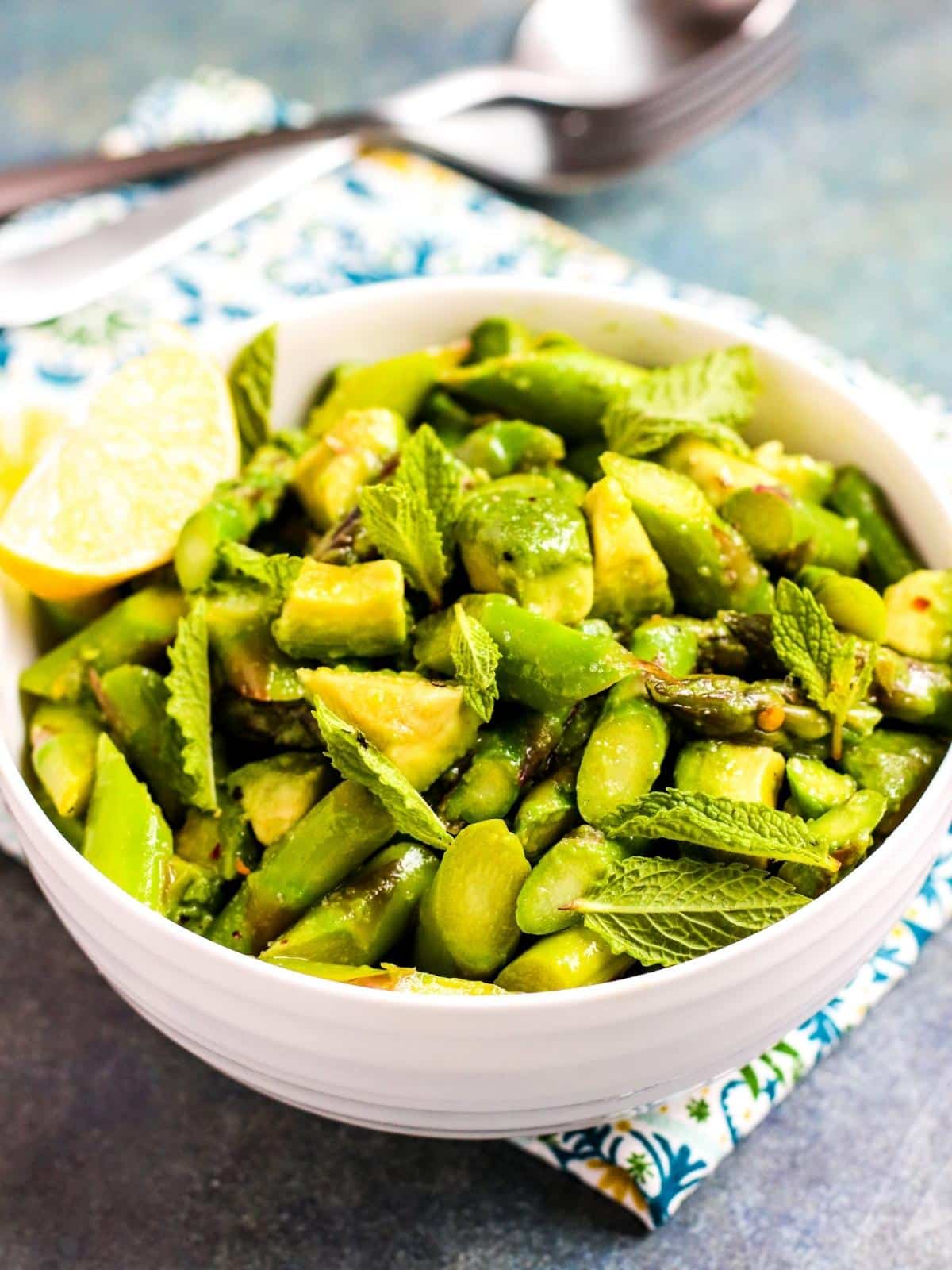 Bowl of Asparagus Avocado Salad with serving utensils in the background.