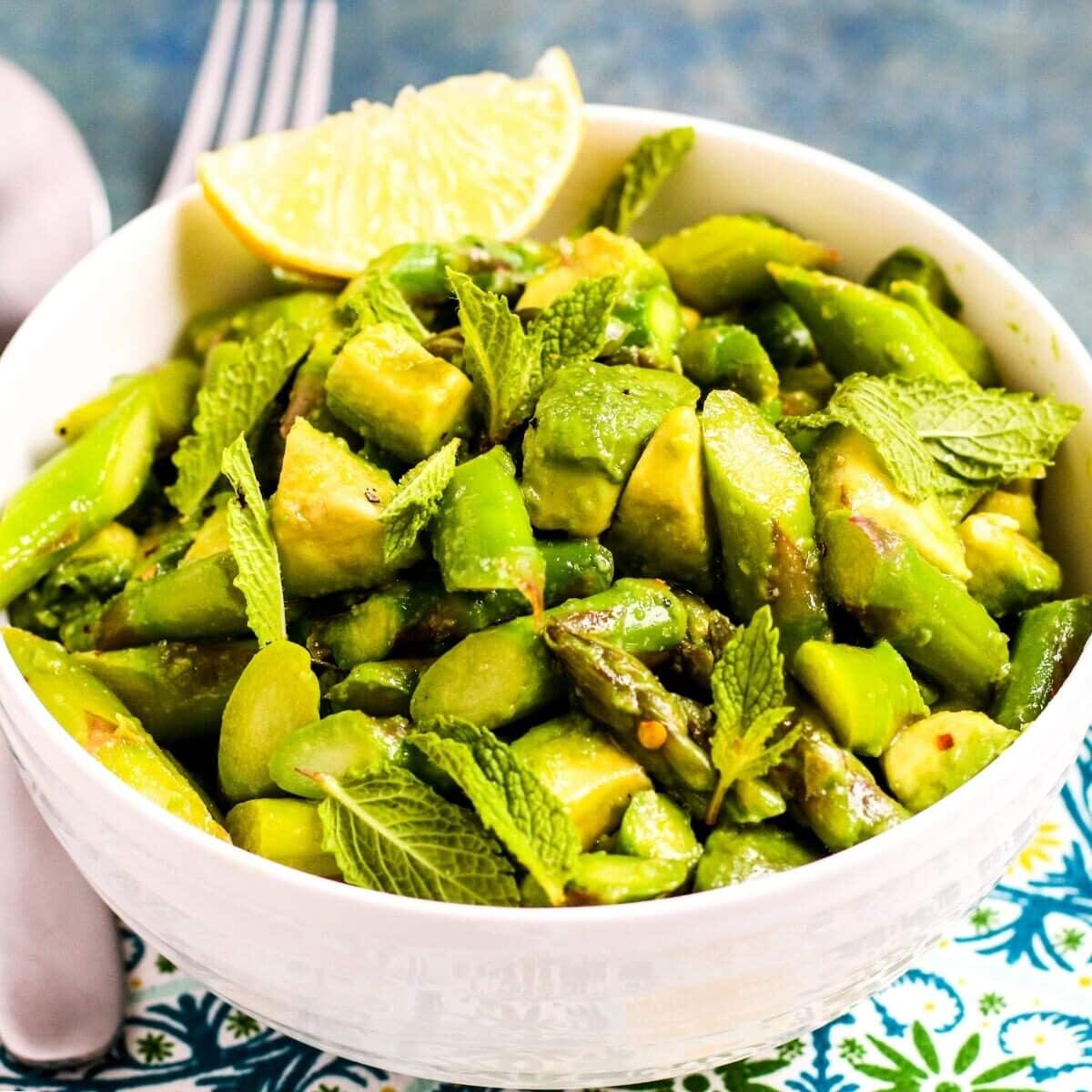 Bowl of Asparagus Avocado Salad garnished with a lime wedge.