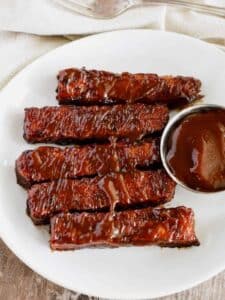 Platter of grilled tempeh with small bowl of barbecue sauce.