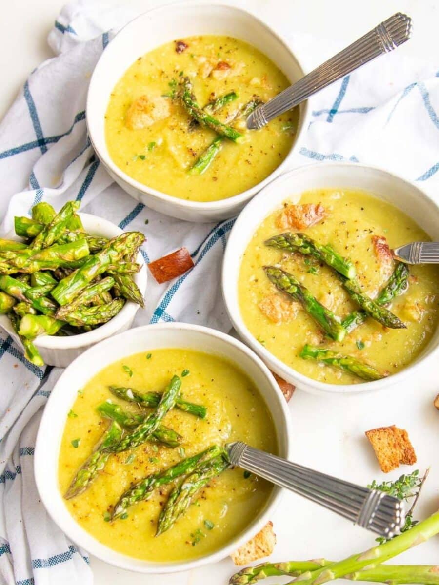 Three bowls of creamy asparagus soup and small bowl of pieces of asparagus.