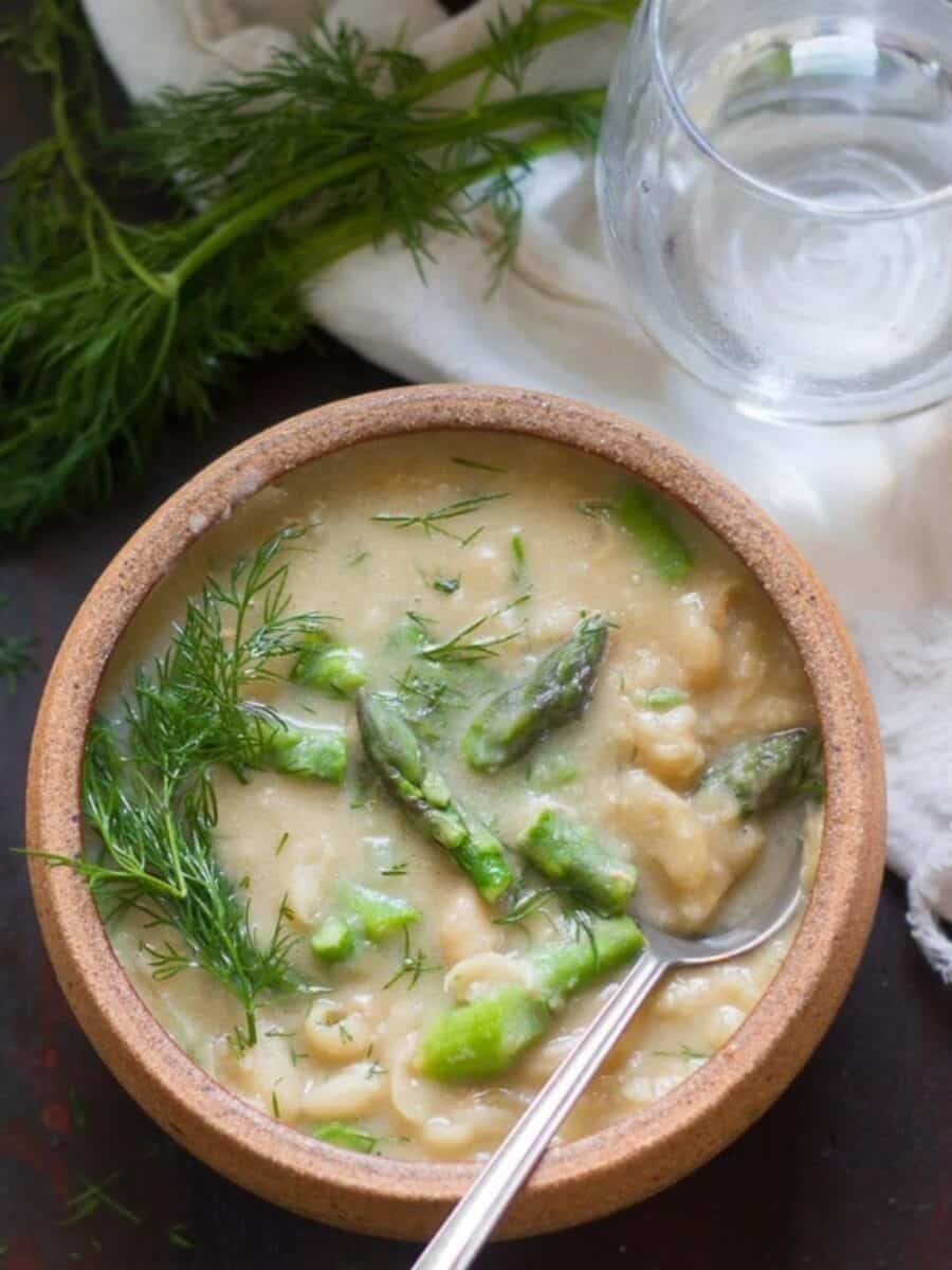 Bowl of White Bean Asparagus Soup with springs of fresh dill and a water glass.