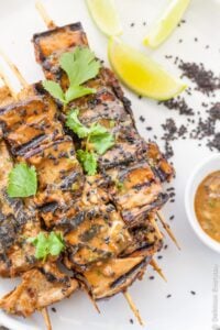 Grilled eggplant on skewers topped with fresh herbs.
