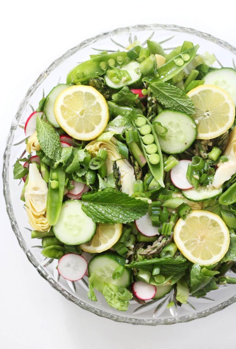 Large bowl of salad with lemon slices, pea pods, asparagus, and radishes.