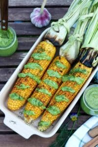 Platter of corn on the cob drizzled with green sauce.