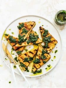 Grilled tofu triangles on a plate drizzled with green sauce.