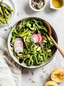 Bowl of green salad with radishes and asparagus.