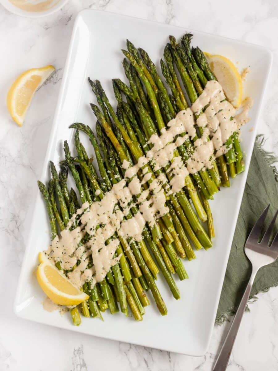 Asparagus on a serving platter drizzled with tahini sauce.