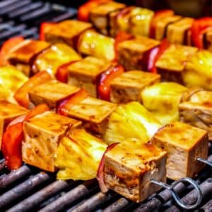 Teriyaki Tofu Skewers with pineapple, red bell pepper, and onion cooking on a barbecue grill.