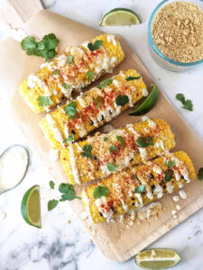 Corn on the cob on a platter topped with herbs, seasoning, and a creamy sauce.