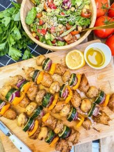 Platter of sausage and veggie skewers next to a bowl of green salad.