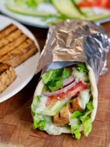 Vegan gyro wrapped in foil next to plate of grilled tofu.