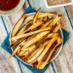 Plate on french fries with small bowls of ketchup and seasoned salt next to it.