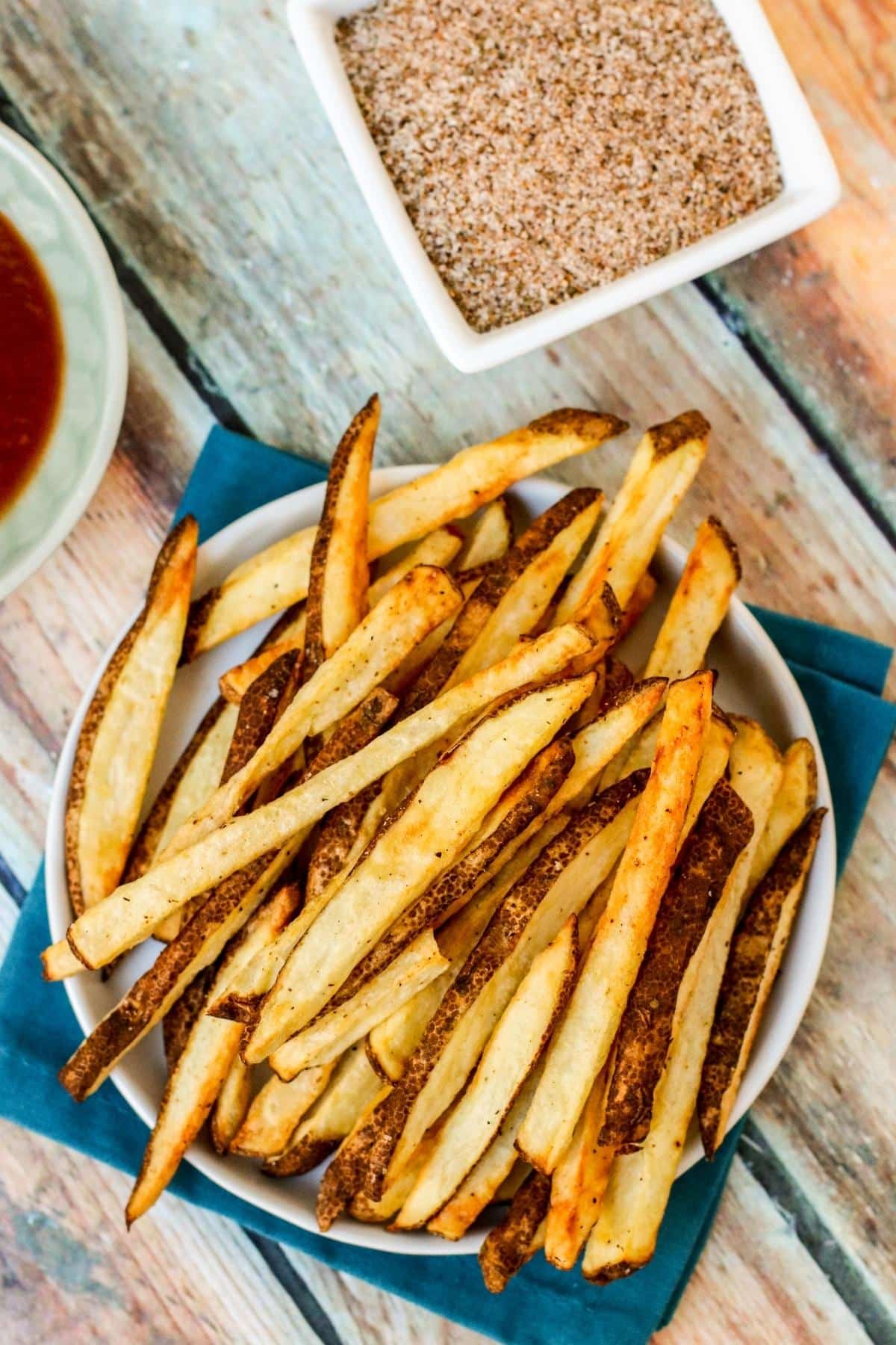 Plate of french fries with small bowls of ketchup and seasoning salt next to it.