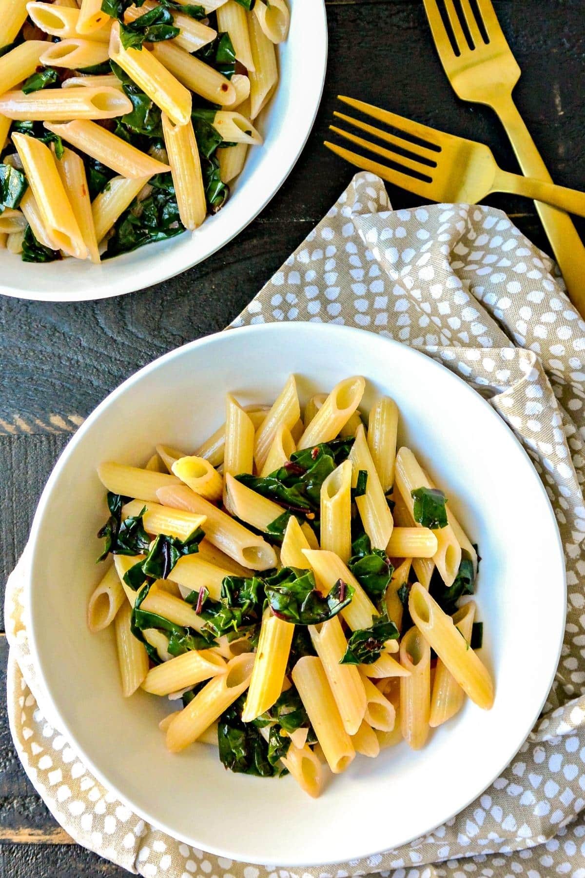 Overhead view of bowls of Swiss chard pasta with gold forks.