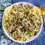 Bowl of artichoke pasta garnished with a lemon slice.