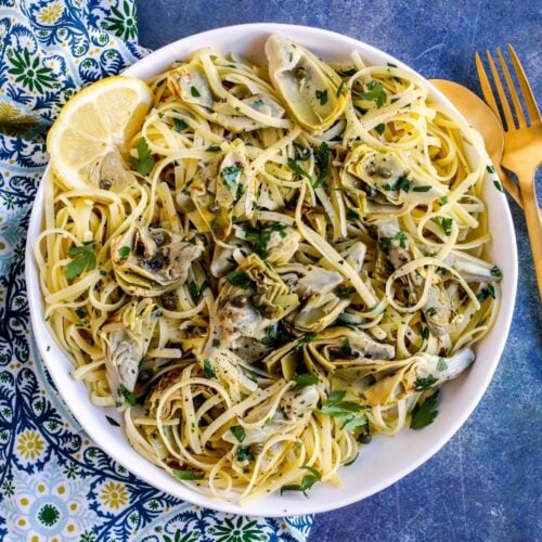 Bowl of artichoke pasta garnished with a lemon slice.