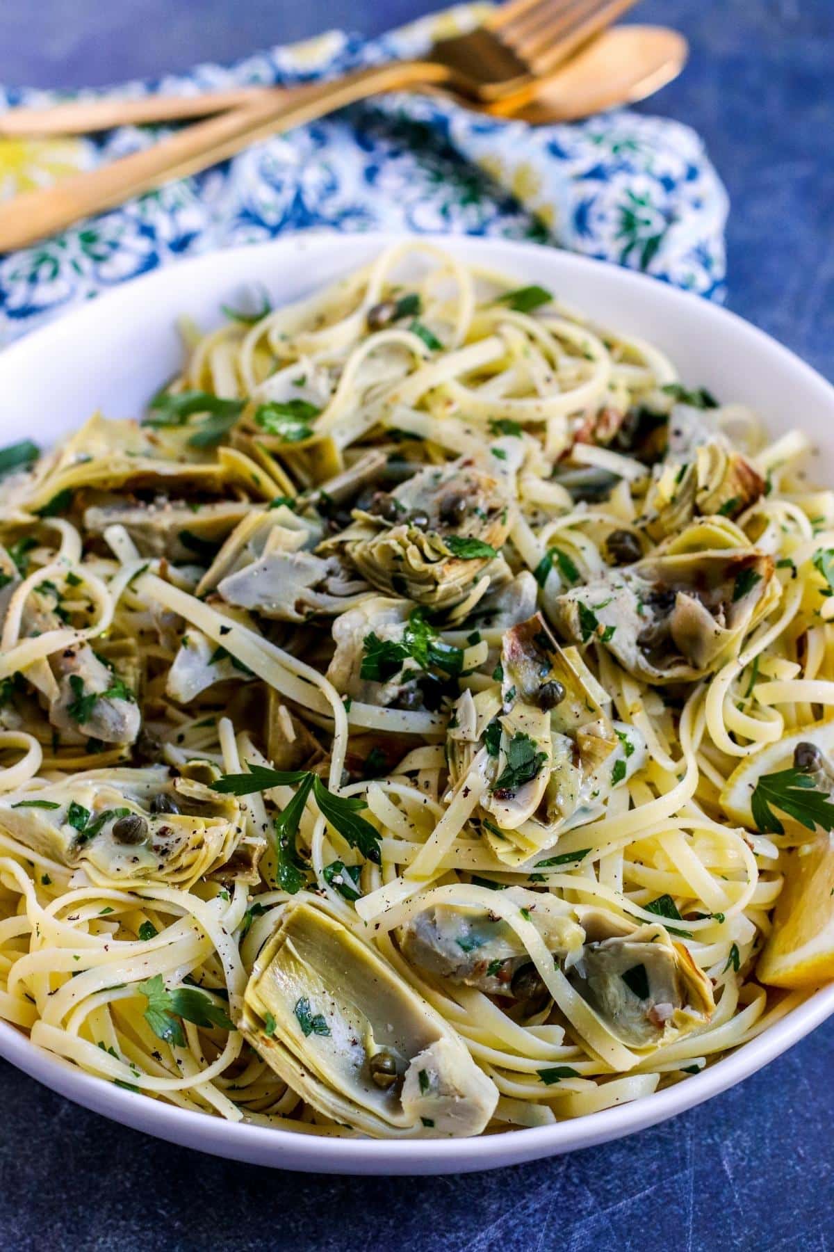 Close up image of plate of artichoke hearts pasta with gold fork and spoon in the background.